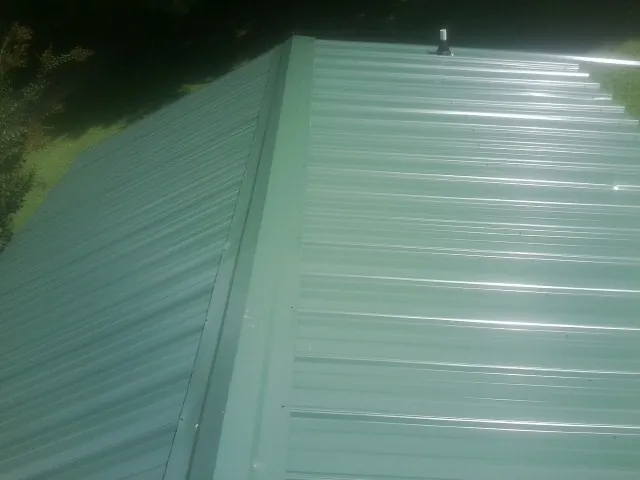 New green metal panels meeting at the ridge of a roof — Flat Roof Repair work by our crew in Kingman