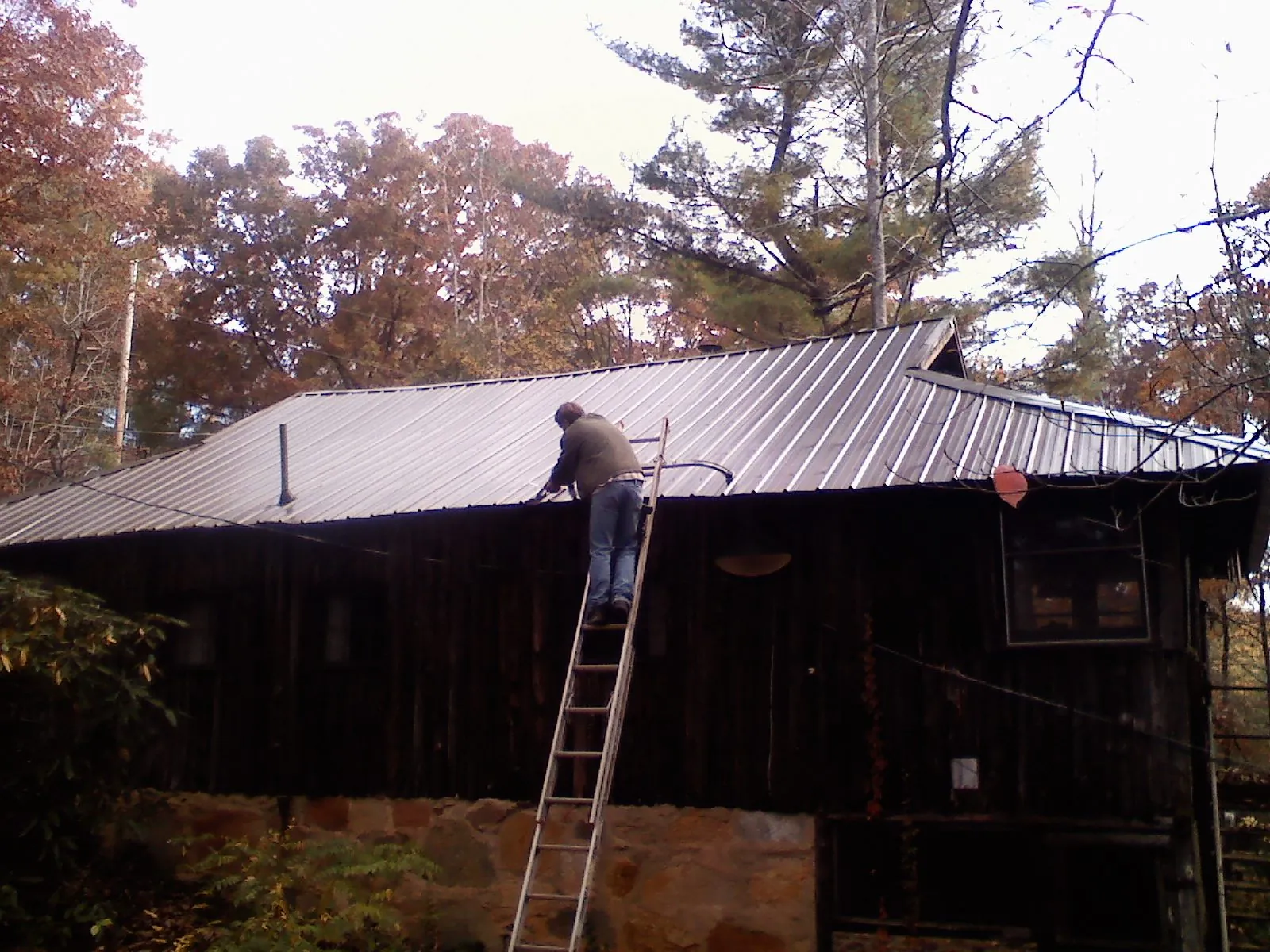 Roofer on a ladder working along the edge of a cabin metal roof in Kingman