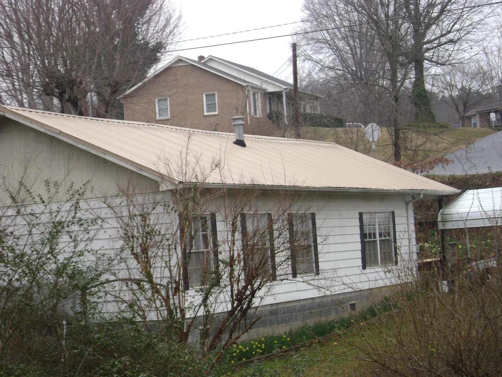 Tan metal roof on a white sided house set into a hillside — Commercial Roofing by Roofing Brothers in Kingman